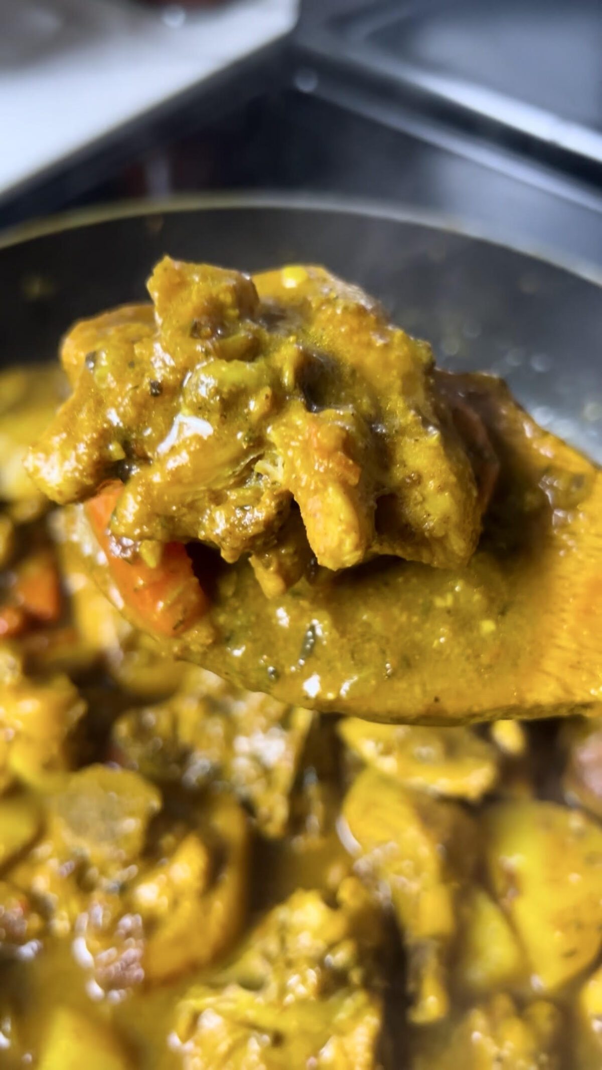 A spoonful of curry chicken held over a pan, showing the thick, well-seasoned curry sauce and tender pieces of chicken.