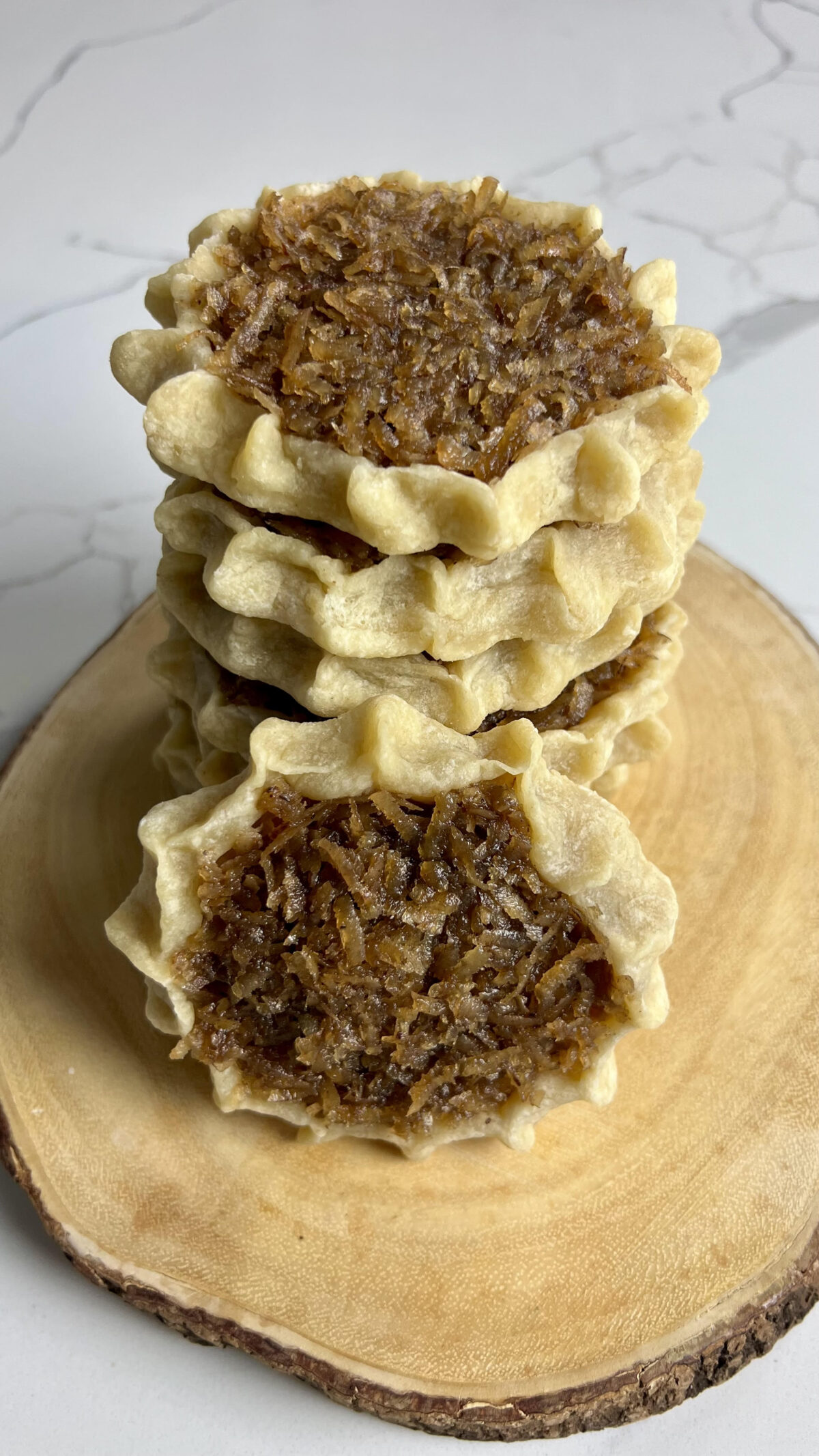 A stack of homemade gizzadas with pinched crust edges and a spiced coconut filling displayed on a wooden board.