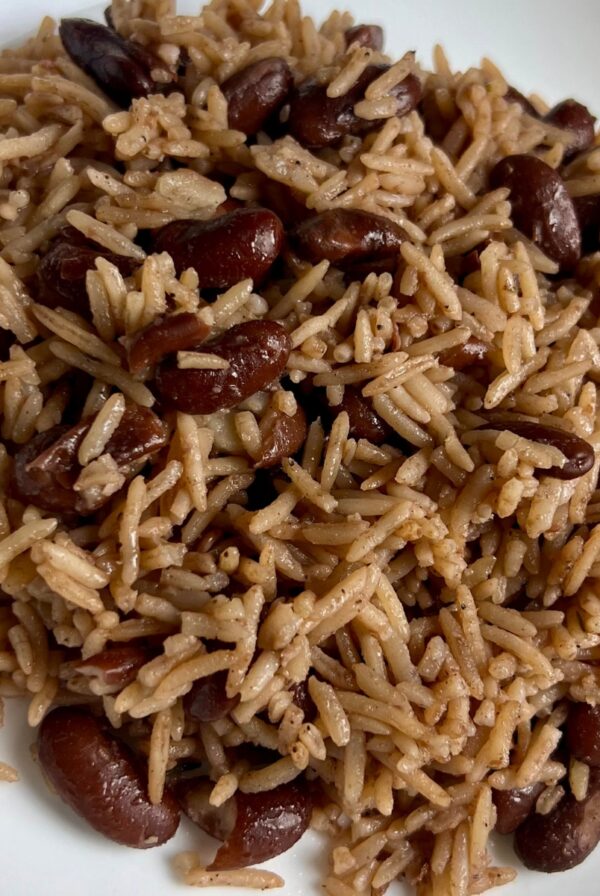 A close-up of Jamaican rice and peas served on a white plate, showing fluffy rice and tender kidney beans.
