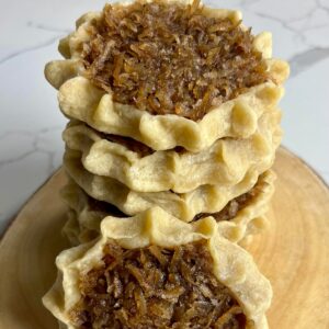 A stack of homemade gizzadas with pinched crust edges and a spiced coconut filling displayed on a wooden board.
