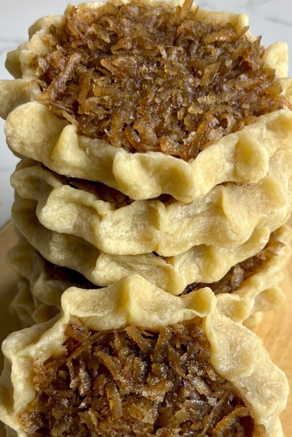 A stack of homemade gizzadas with pinched crust edges and a spiced coconut filling displayed on a wooden board.