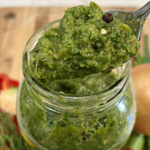 A spoon scooping vibrant Caribbean green seasoning from a jar, highlighting its chunky texture and fresh herb blend.