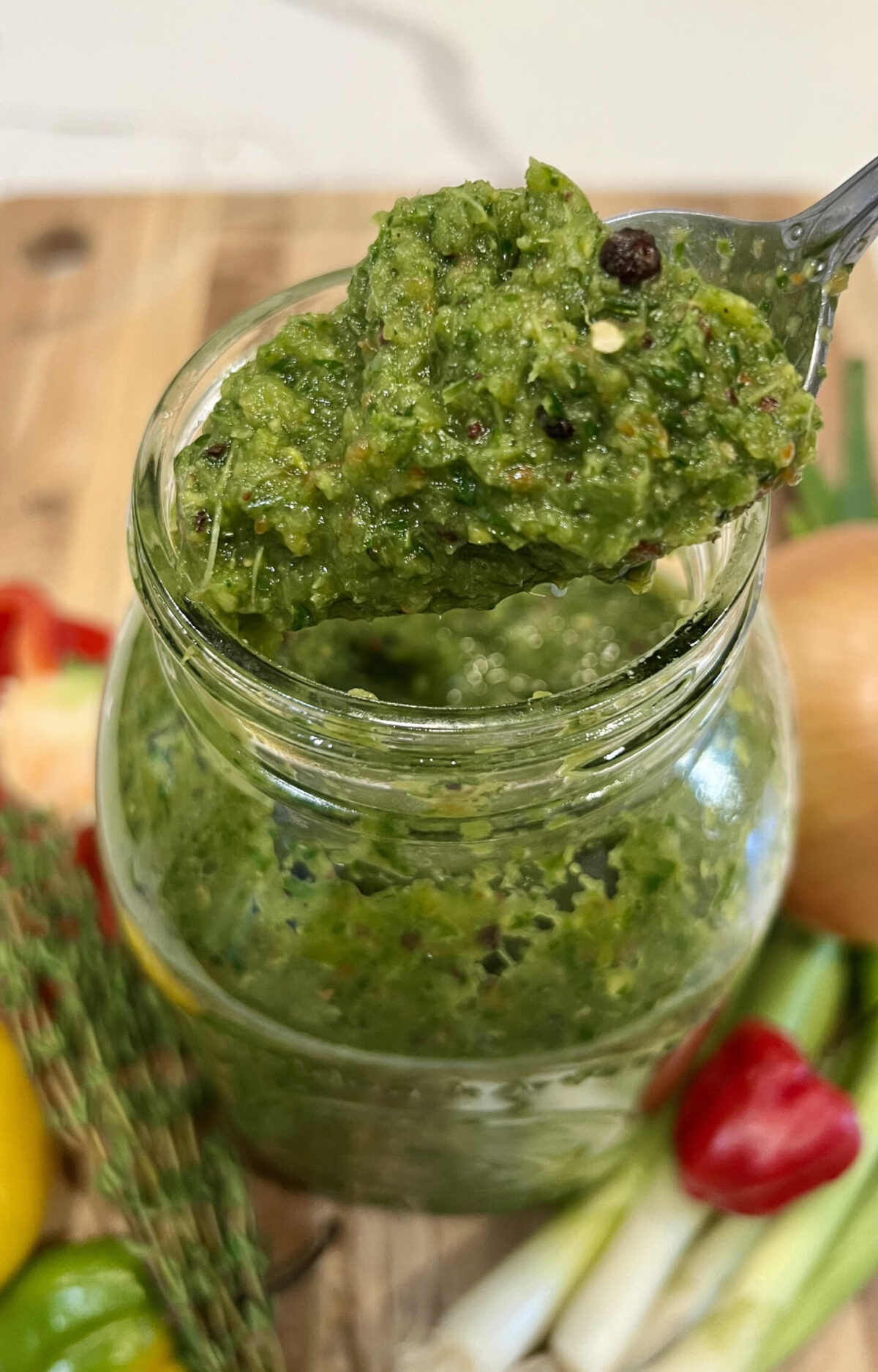 A spoon scooping vibrant Caribbean green seasoning from a jar, highlighting its chunky texture and fresh herb blend.