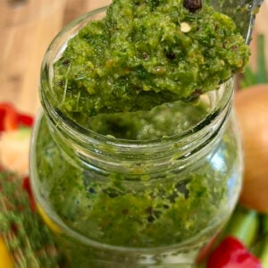 A spoon scooping vibrant Caribbean green seasoning from a jar, highlighting its chunky texture and fresh herb blend.