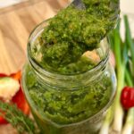 A spoonful of freshly blended green seasoning being lifted from a jar, showing its thick, textured consistency.
