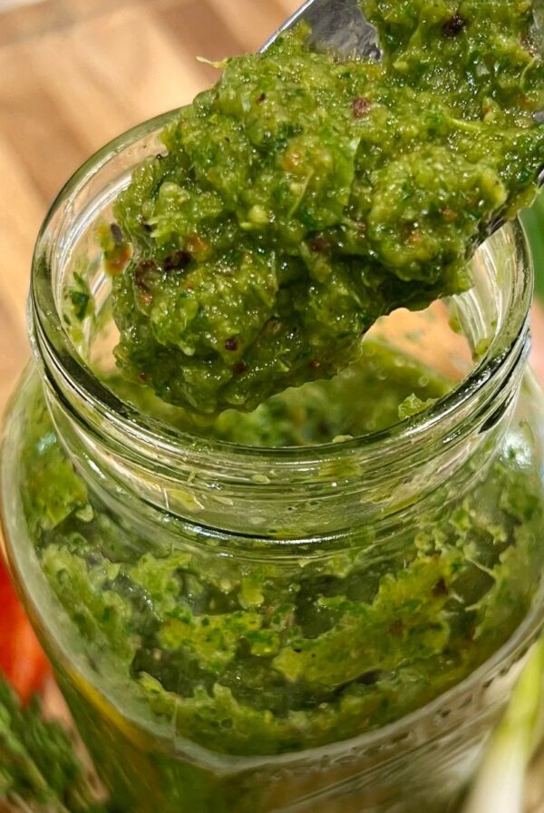 A spoonful of freshly blended green seasoning being lifted from a jar, showing its thick, textured consistency.