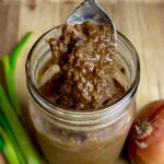 A spoon lifting thick, blended Jamaican jerk marinade from a jar, showing its rich, textured consistency.