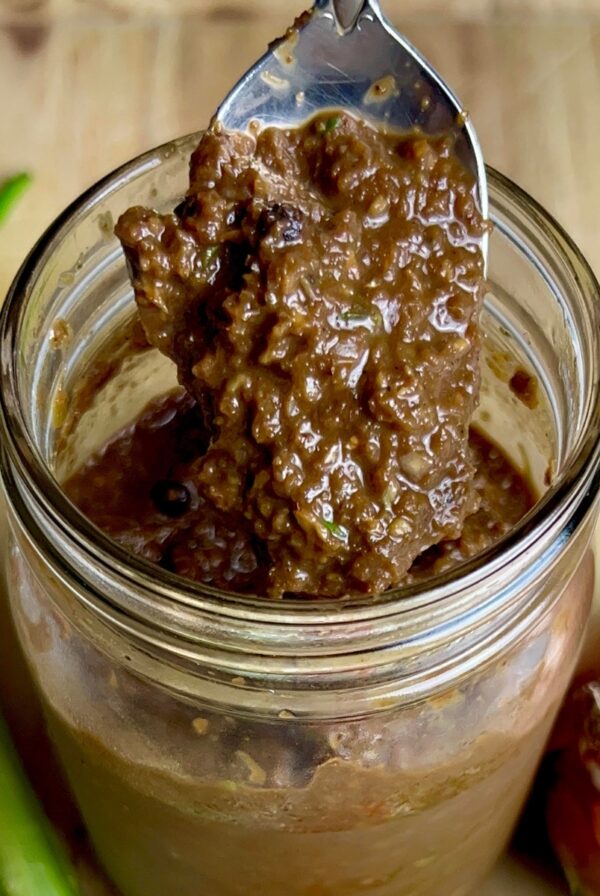 A spoon lifting thick, blended Jamaican jerk marinade from a jar, showing its rich, textured consistency.