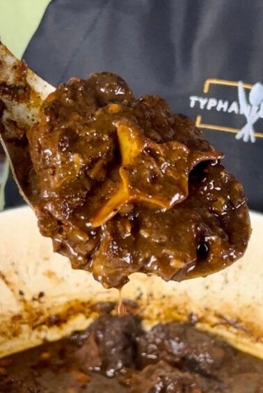 Close-up of a spoonful of braised oxtail with deep brown gravy held over a pot, with the Typhanie Cooks logo visible in the background.