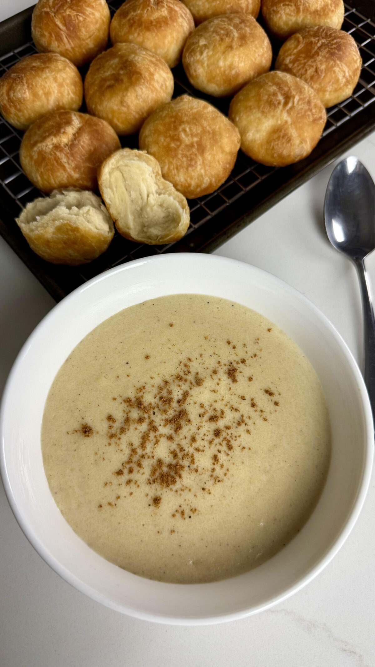 A bowl of creamy cornmeal porridge sprinkled with spice, paired with golden fried dumplings in the background on a cooling rack.