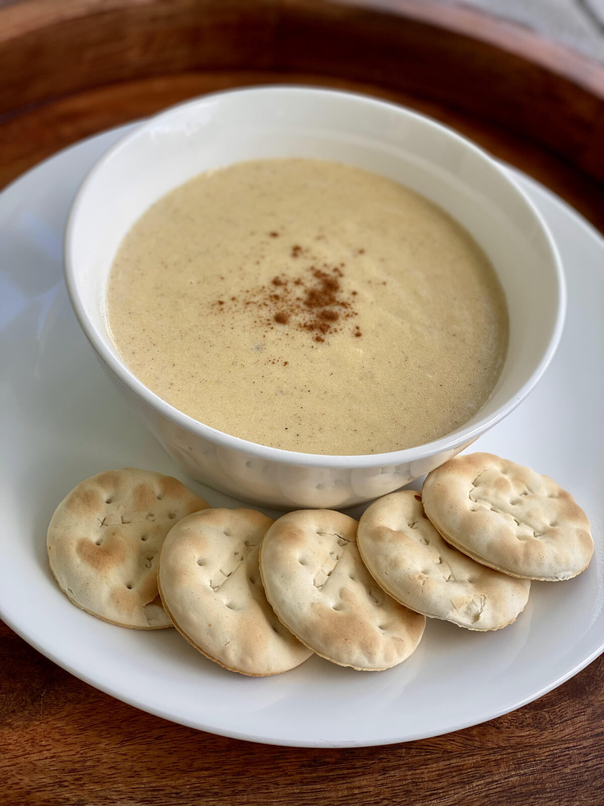 A close-up of smooth, creamy cornmeal porridge in a white bowl with a light dusting of spice on top, served alongside water crackers.