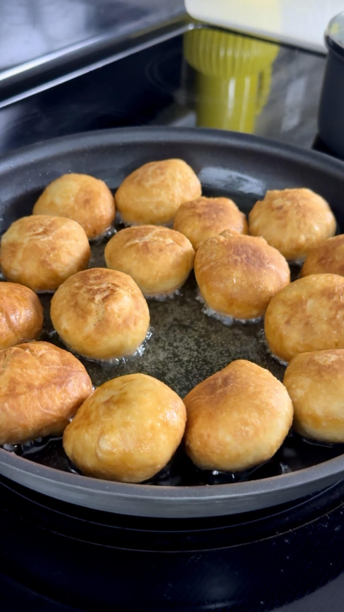 Jamaican dumplings frying in hot oil in a skillet, bubbling as they turn golden brown on all sides.