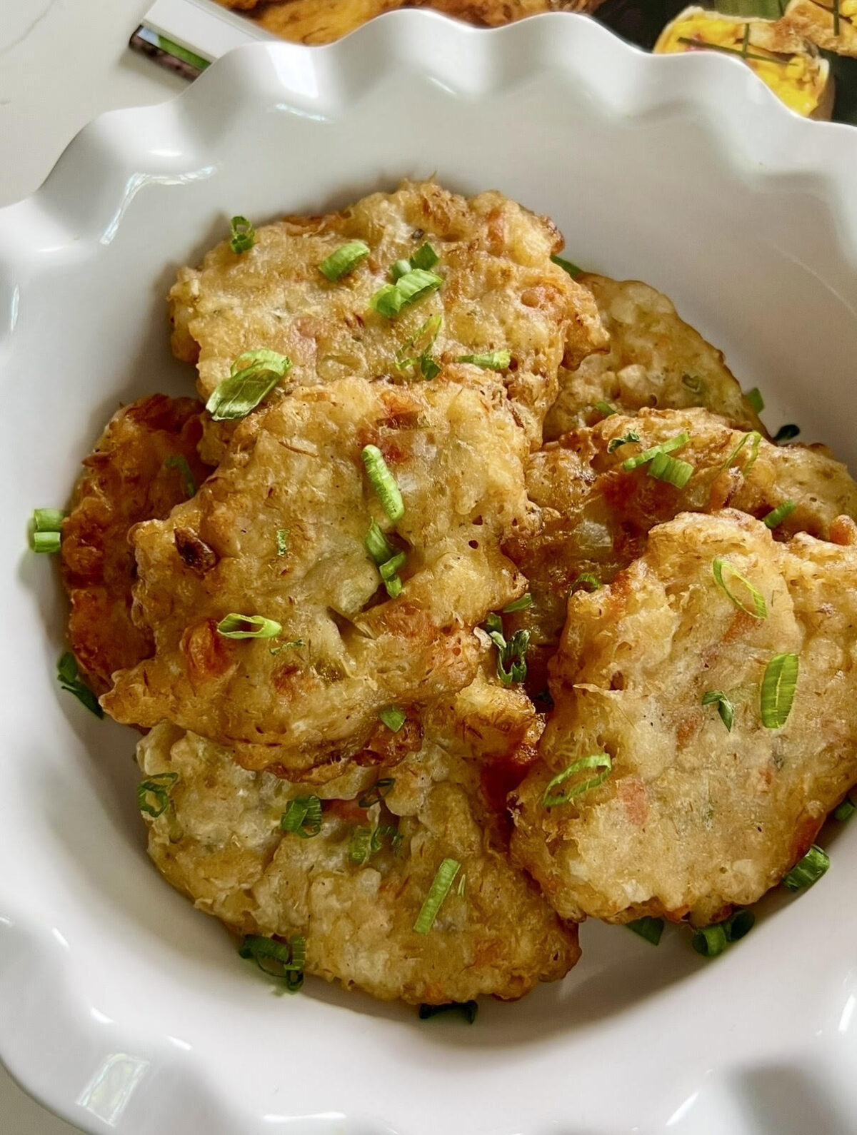 Golden fried saltfish fritters served in a white bowl with a light sprinkle of chopped green onions.