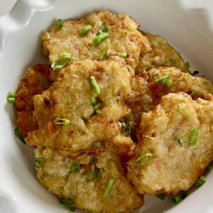 Golden fried saltfish fritters served in a white bowl with a light sprinkle of chopped green onions.