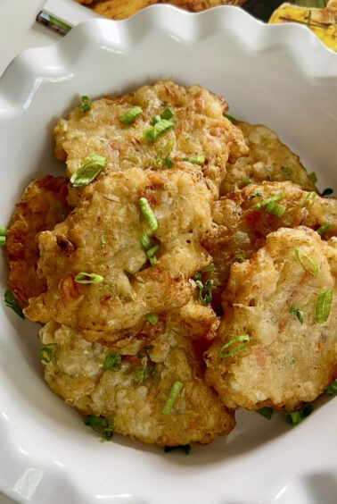 Golden fried saltfish fritters served in a white bowl with a light sprinkle of chopped green onions.