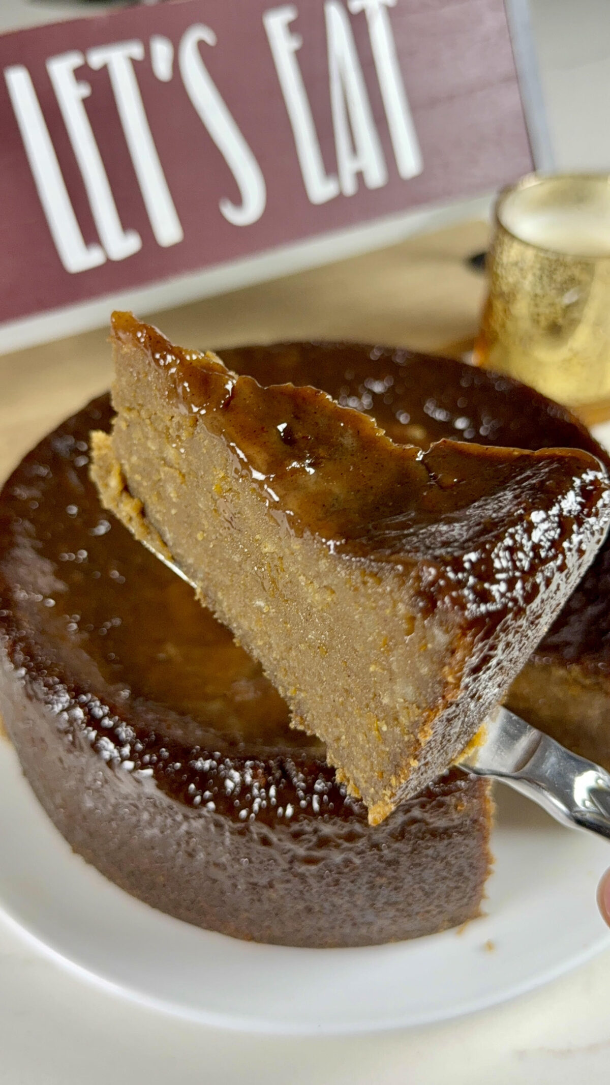 A slice of sweet potato pudding held above the full pudding, highlighting its rich texture with a shiny, caramelized top.