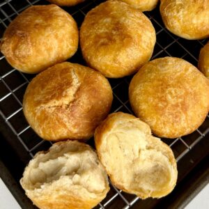 Golden brown Jamaican fried dumplings cooling on a wire rack with one dumpling broken open to show the soft, fluffy center.
