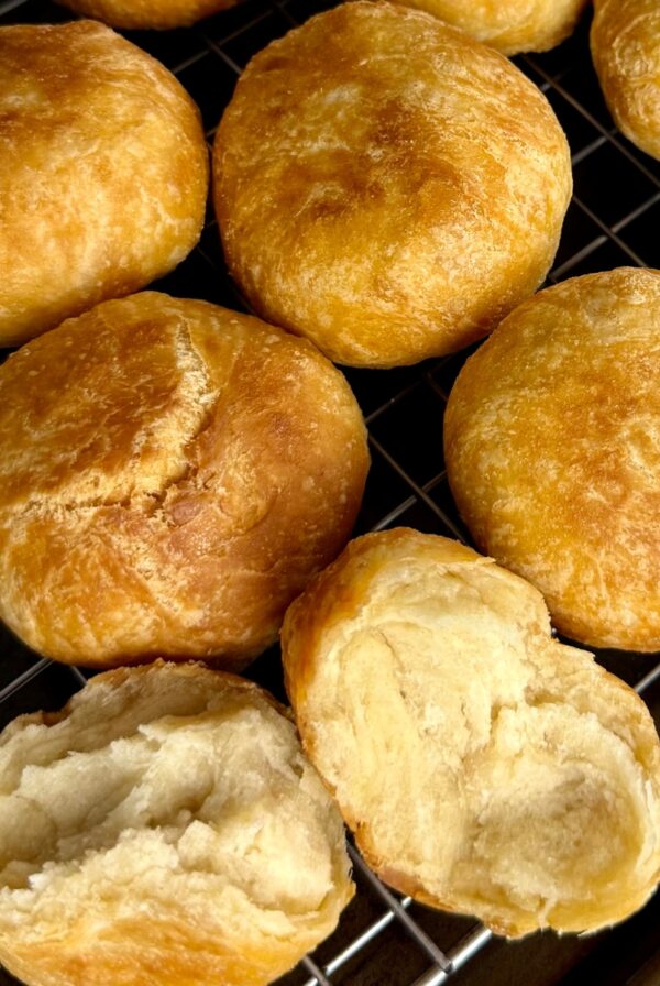 Golden brown Jamaican fried dumplings cooling on a wire rack with one dumpling broken open to show the soft, fluffy center.