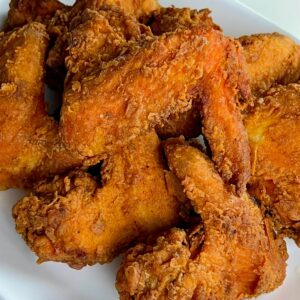 Golden brown whole fried chicken wings with a crisp coating served on a white plate.
