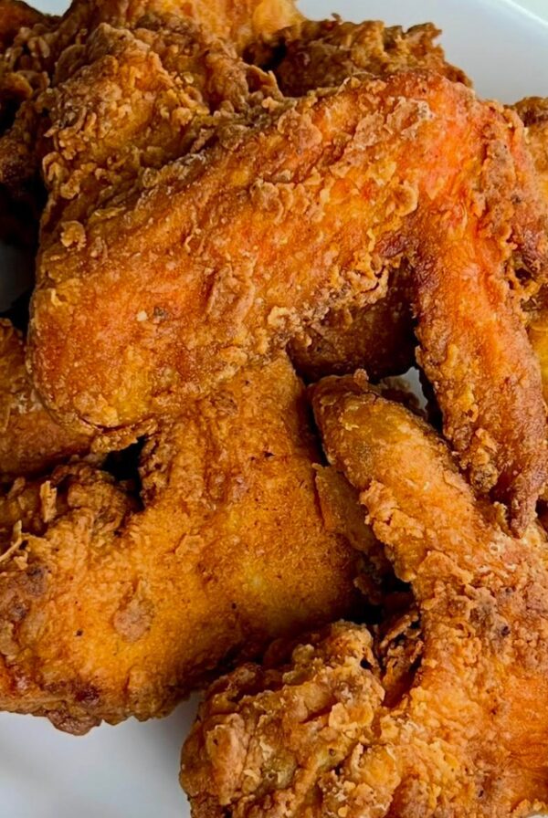 Golden brown whole fried chicken wings with a crisp coating served on a white plate.