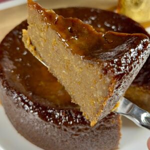 A close-up of a slice of Jamaican sweet potato pudding being lifted on a fork, showing its dense interior and glossy dark top.