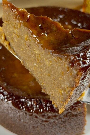 A close-up of a slice of Jamaican sweet potato pudding being lifted on a fork, showing its dense interior and glossy dark top.