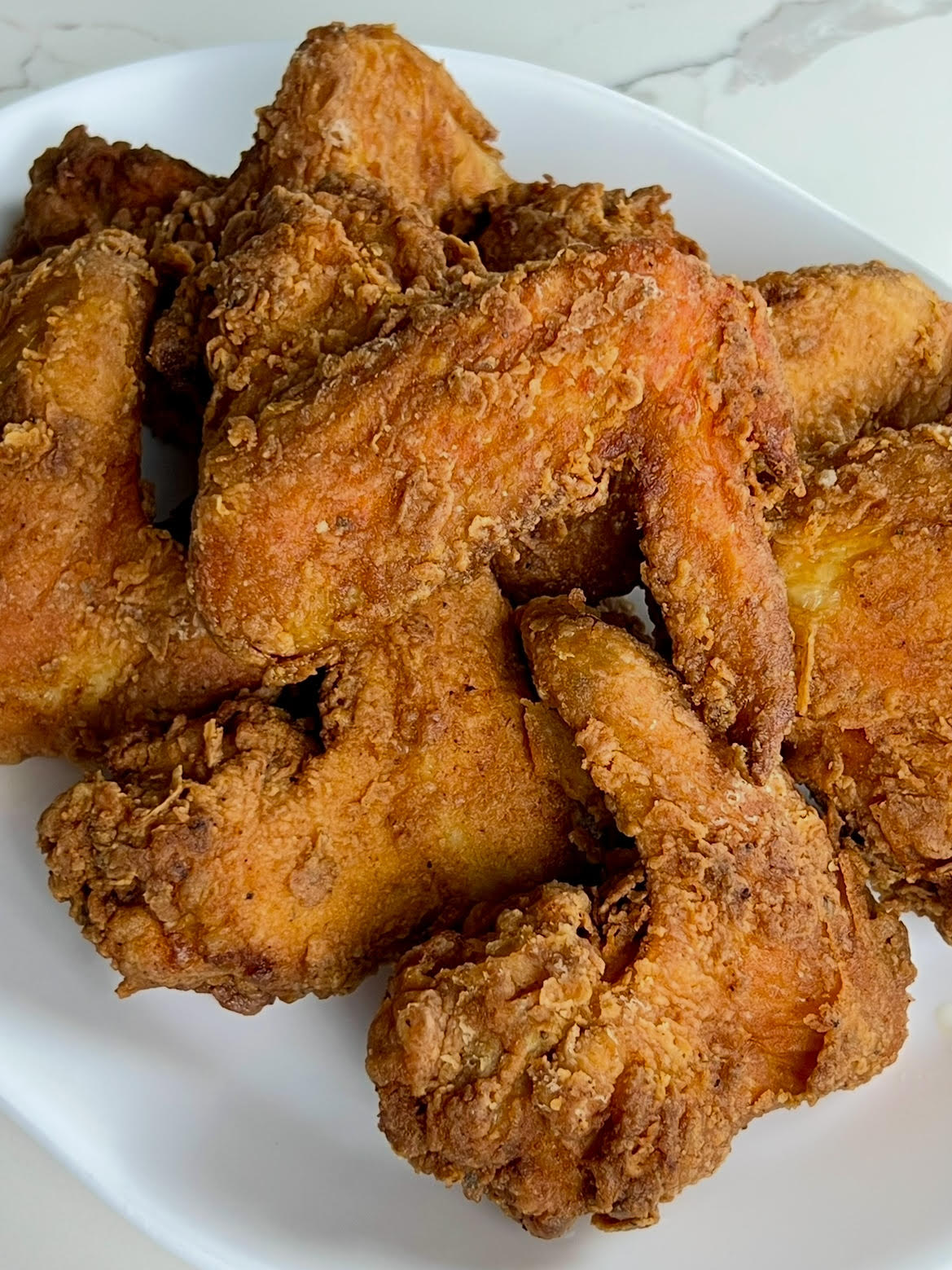 Crispy whole fried chicken wings with a well-seasoned coating arranged on a white plate.