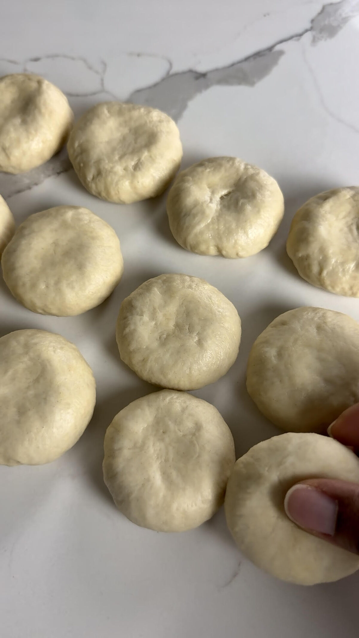 Raw, shaped dumpling dough pieces arranged on a surface, with one being gently pressed to flatten before frying.