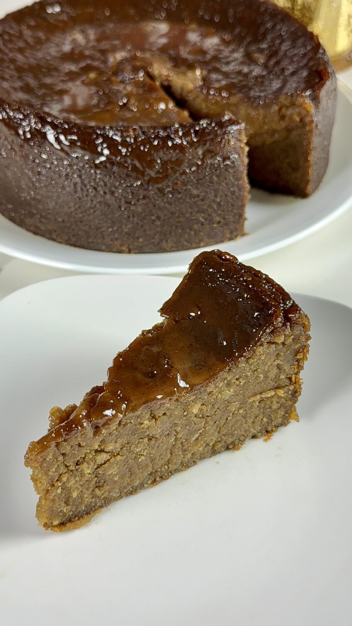 A sliced piece of sweet potato pudding in the foreground with the remaining pudding behind it, showing the dense interior and smooth top.