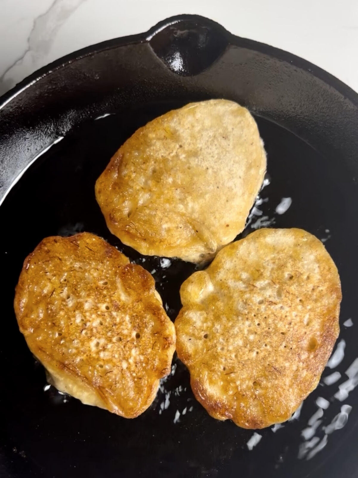 Freshly fried Jamaican banana fritters cooking in a cast iron skillet until golden brown and crisp around the edges.