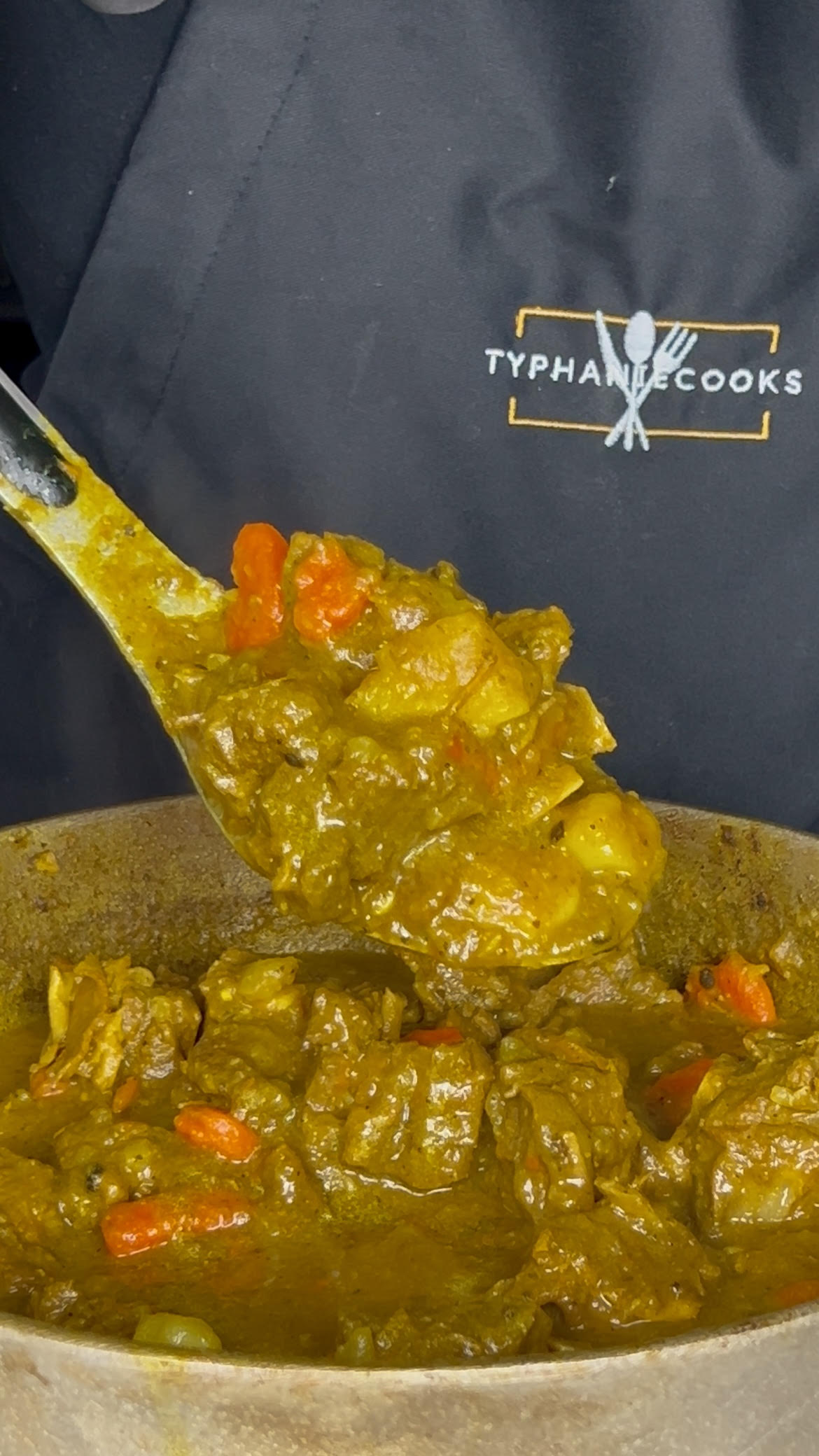 Close-up of Jamaican curry goat simmering in a curry gravy with potatoes and carrots in a Dutch oven.