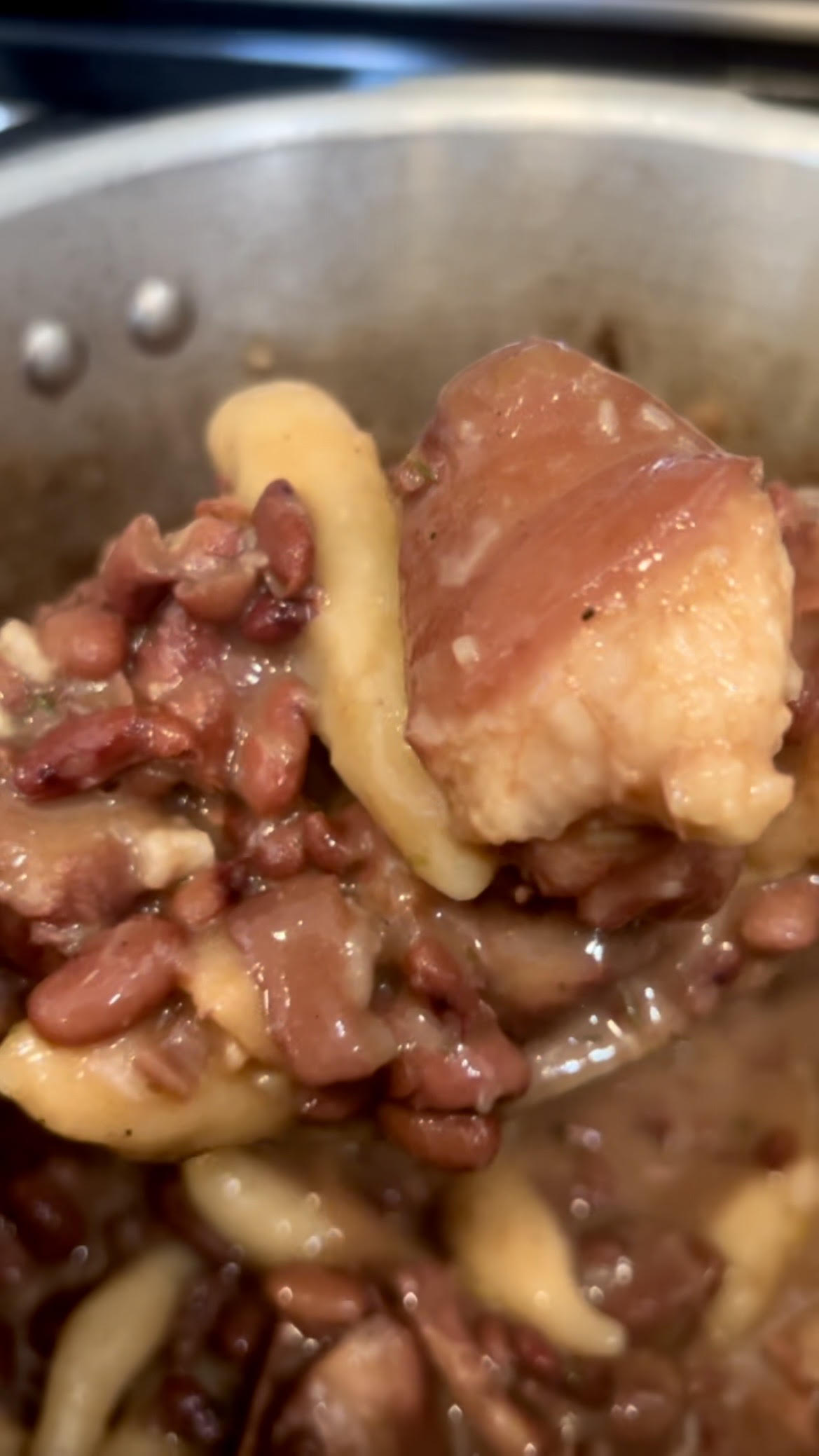 Spoonful of Jamaican stew peas with salted pigtail, red beans, and homemade spinners lifted from the pot.