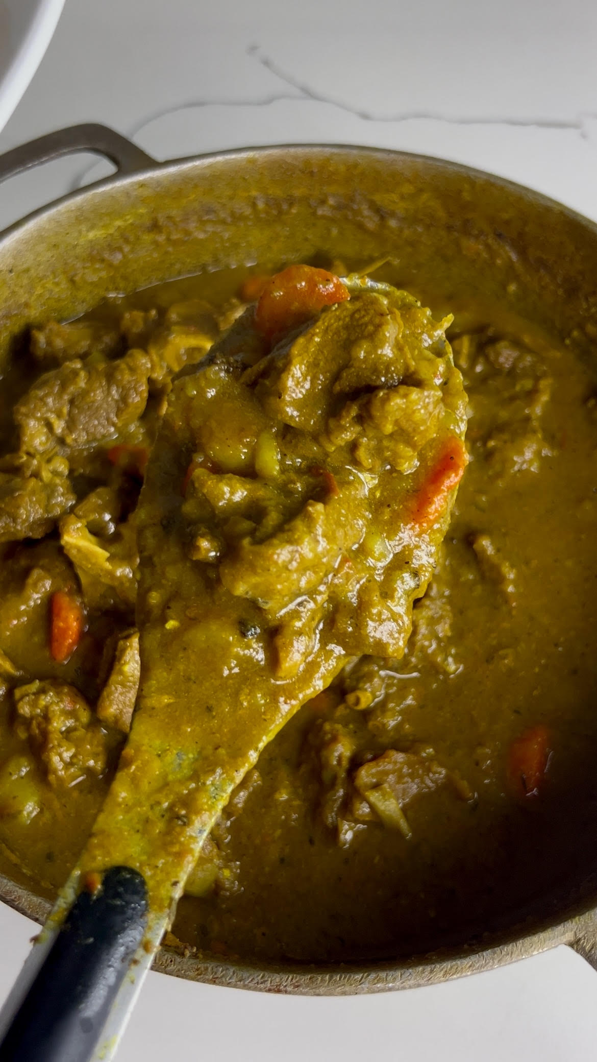 Thick and flavorful Jamaican curry goat with tender meat, potatoes, and carrots simmering in a rich curry sauce.