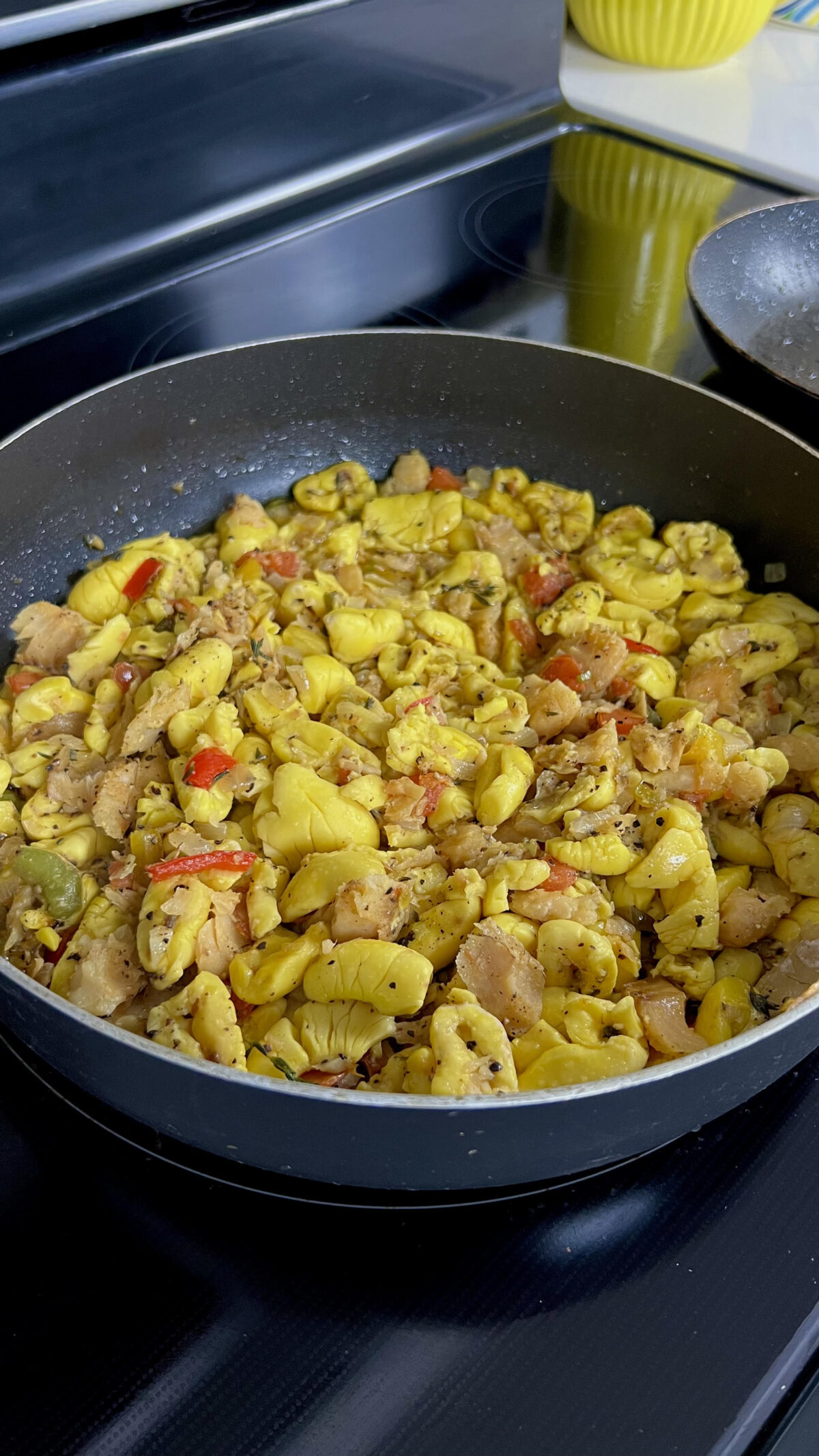 Skillet filled with ackee and saltfish cooked with onions, peppers, tomatoes, and herbs on a stovetop.