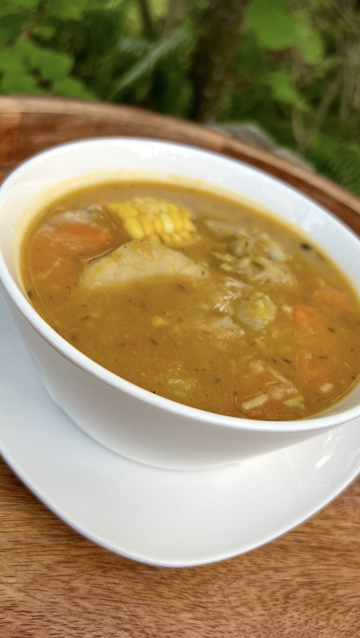A close-up of Jamaican chicken soup filled with chicken, corn, carrots, and dumplings in a rich golden broth.