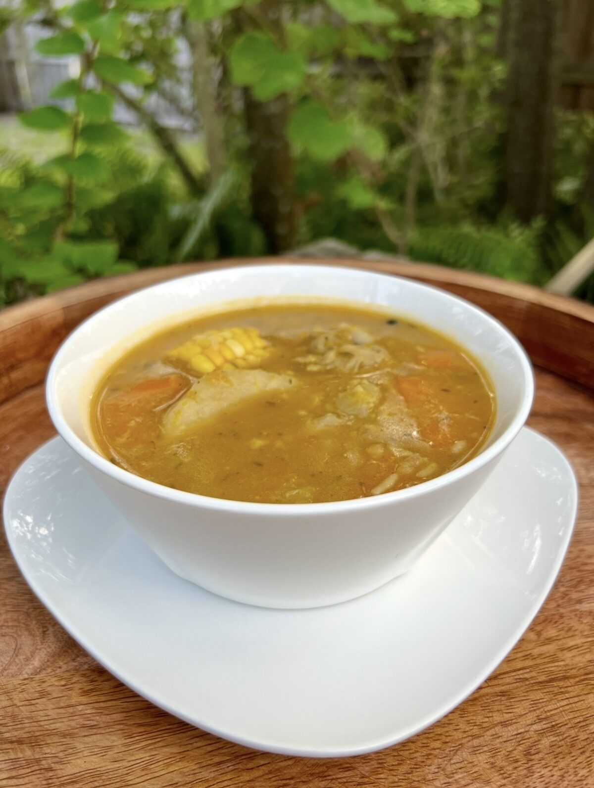 A bowl of Jamaican chicken soup with chicken, corn, carrots, and dumplings served outdoors.