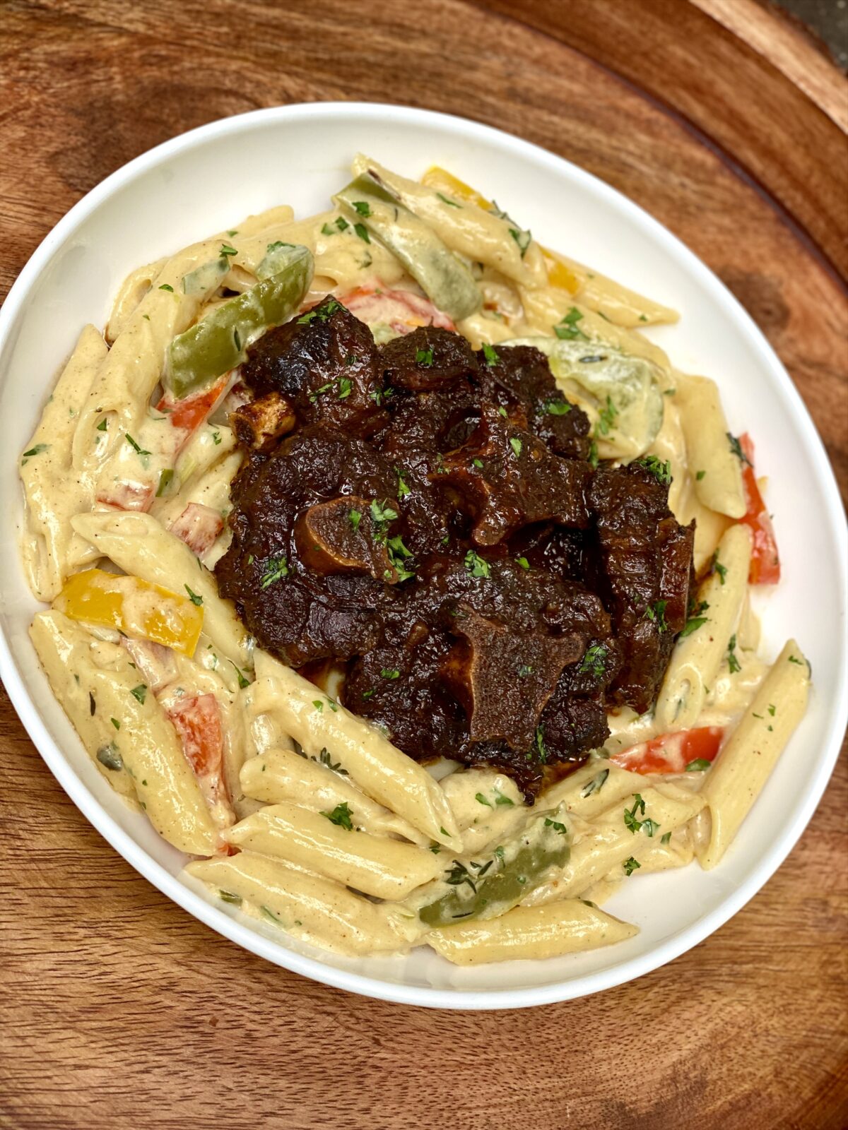 Creamy Rasta Pasta with penne and colorful bell peppers topped with oxtail and chopped parsley.