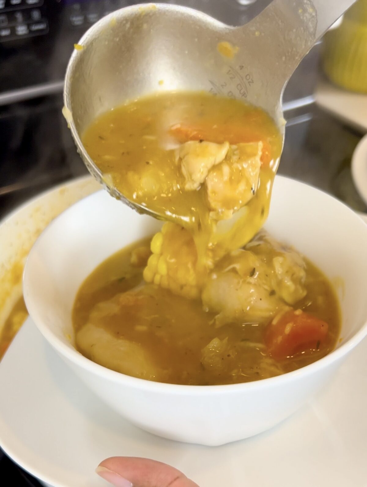 Jamaican chicken soup being ladled into a bowl with chicken, corn, carrots, dumplings, and golden broth.