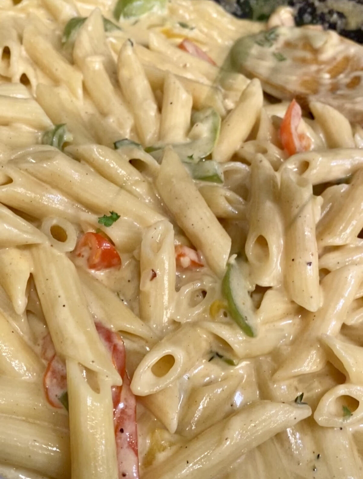 Close-up of creamy Rasta Pasta with penne, sliced red and green bell peppers, and herbs.