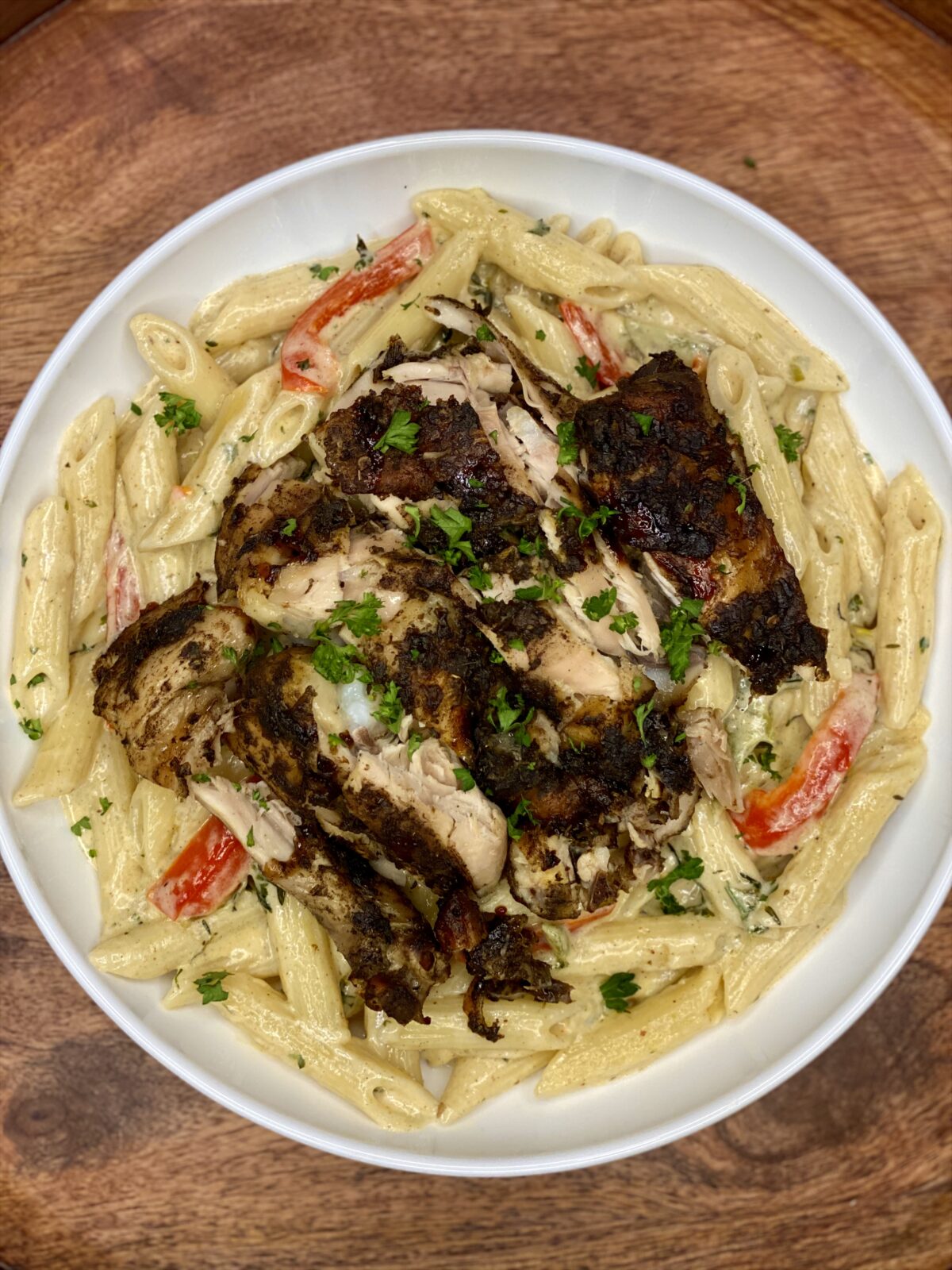 Creamy Rasta Pasta with penne and sliced bell peppers topped with jerk chicken and chopped parsley.