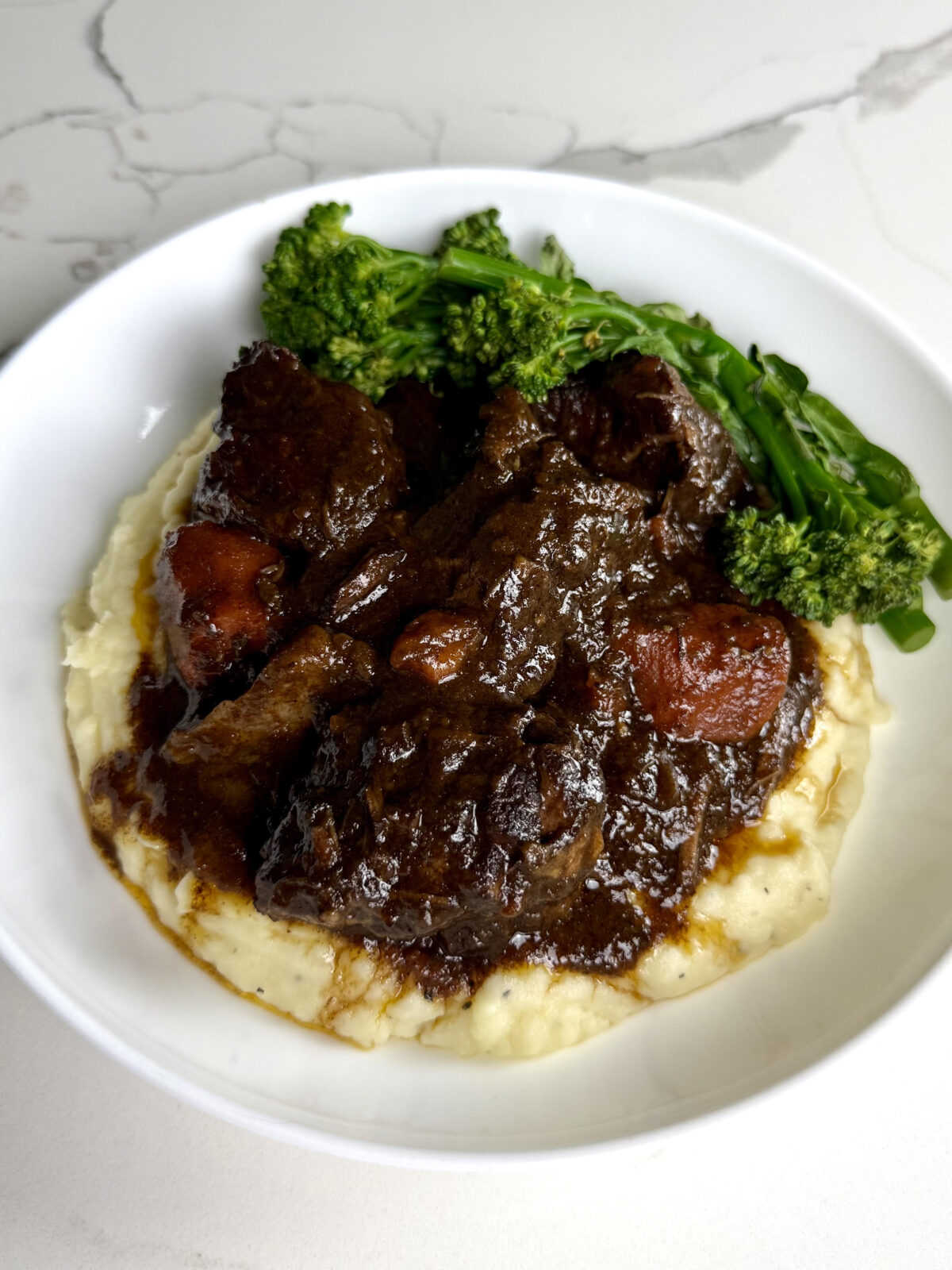 Red wine braised beef and carrots in a rich gravy are served over creamy mashed potatoes with steamed broccolini.