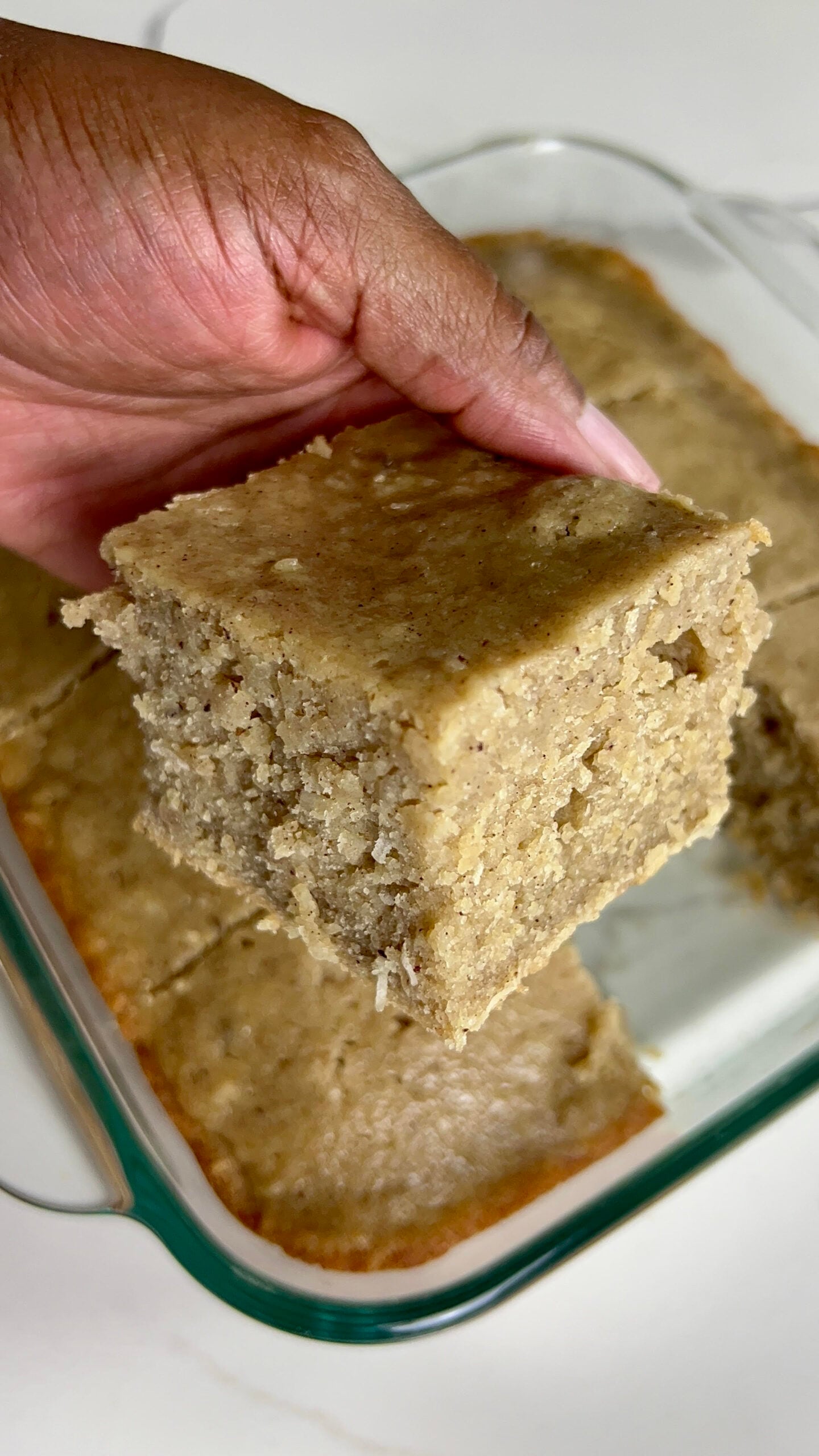 A slice of Jamaican Toto (Coconut Cake) in hand, ready to eat.