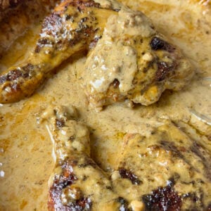 Chicken au poivre in a pan with plenty of creamy black pepper sauce.